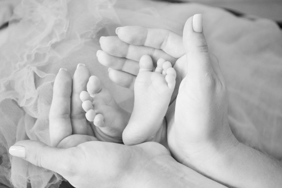 Adult hands gently holding a baby's feet, a tender moment of early motherhood