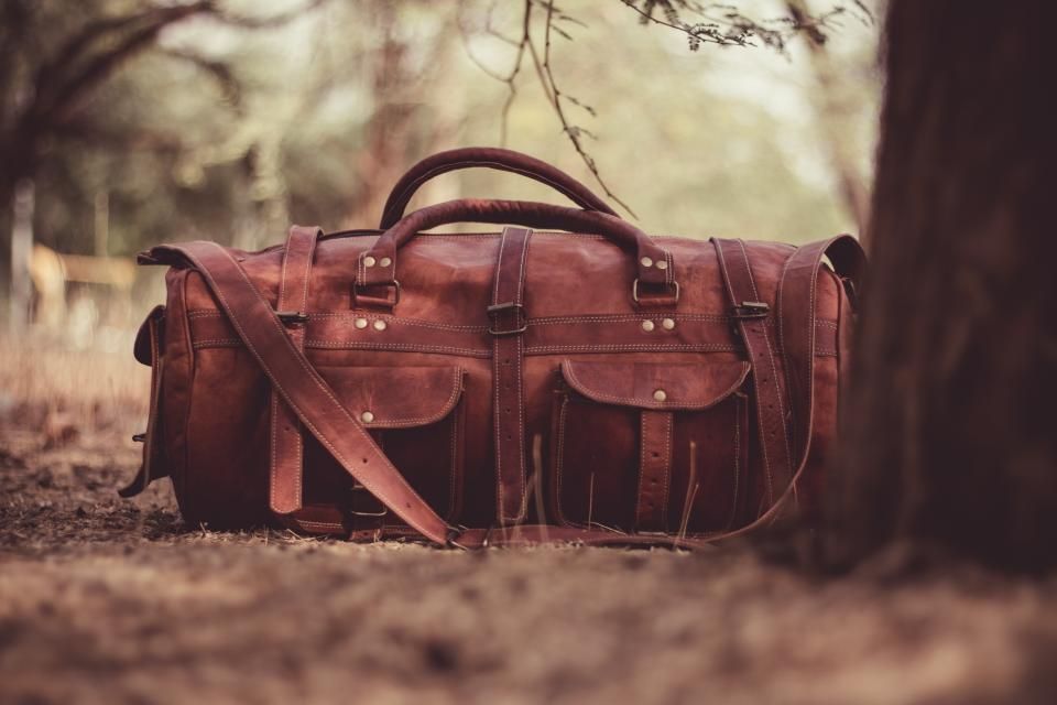 Brown leather travel bag with front pockets sitting on the ground