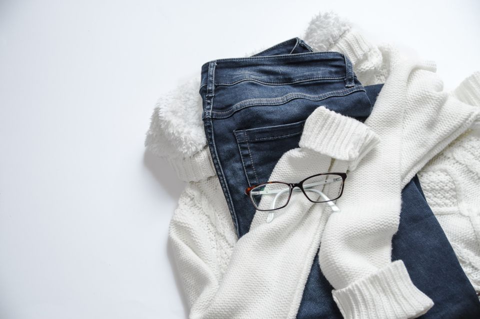 Flat lay of dark jeans and a cream knit sweater for a casual mom outfit