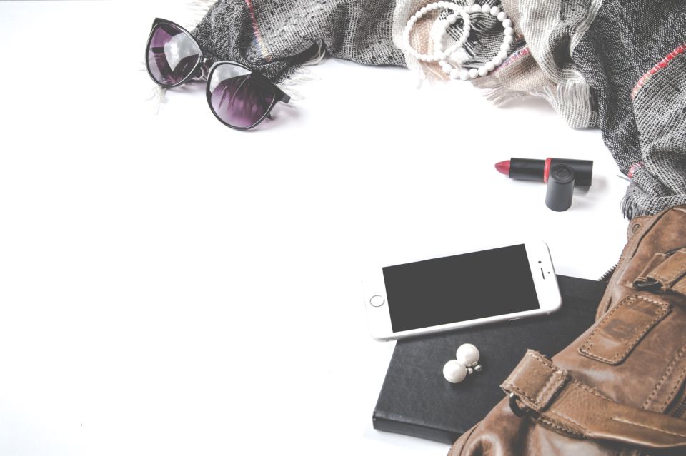 Flat lay of sunglasses, lipstick, phone and a small bag on a white background
