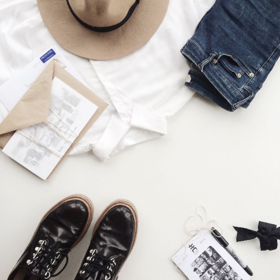 Flat lay of white shirt, jeans, hat and dark shoes, essentials for a simple capsule wardrobe