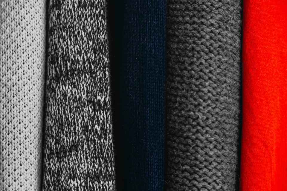 Folded knit sweaters in grey, black, navy and red, showing a neutral palette with one accent
