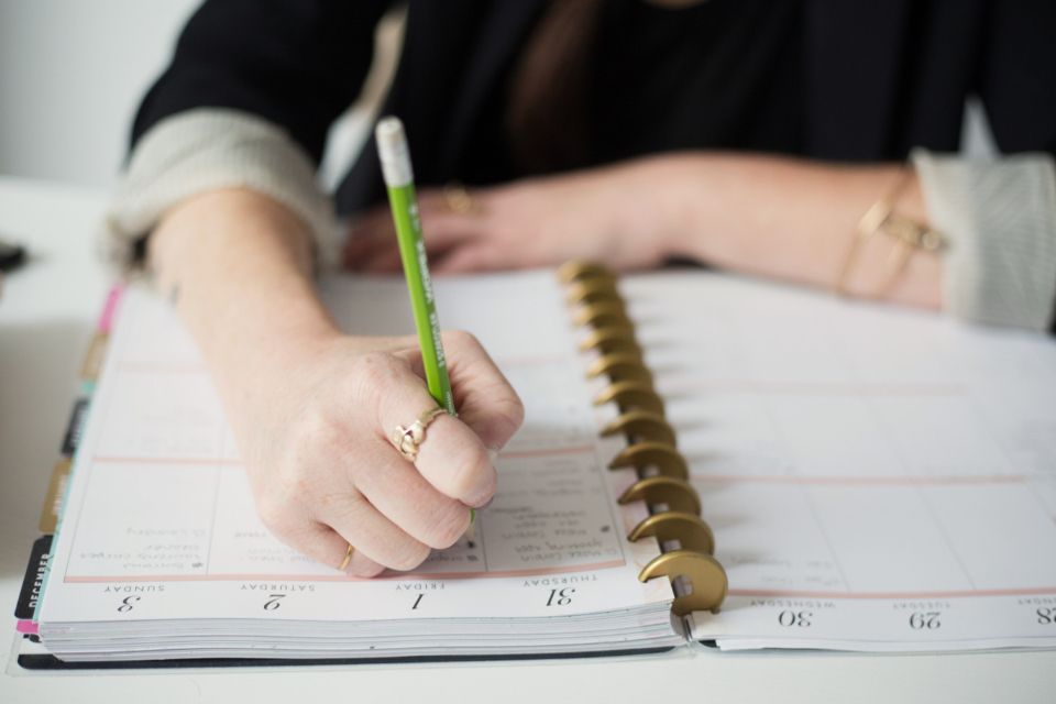 Hand writing in a planner with a green pen, a work bag essential