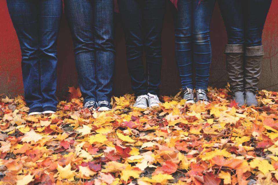 Legs in jeans and sneakers standing among autumn leaves