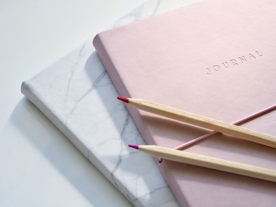 Pink journal with coloured pencils on a marble surface