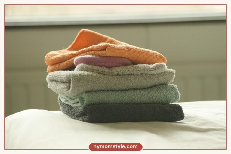 Stack of soft folded clothes in pastel colours on a bed, postpartum wardrobe essentials