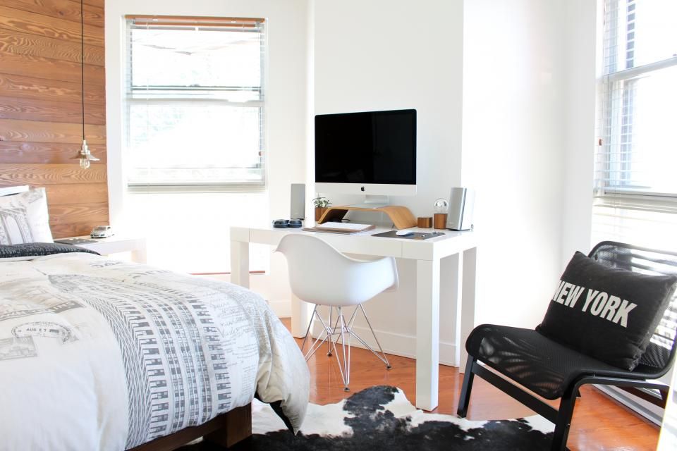 Small home office in a bedroom with a white desk, computer and window light