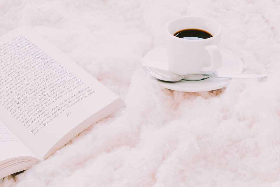 Soft pink blanket with a cup of coffee and an open book, a cosy postpartum recovery moment