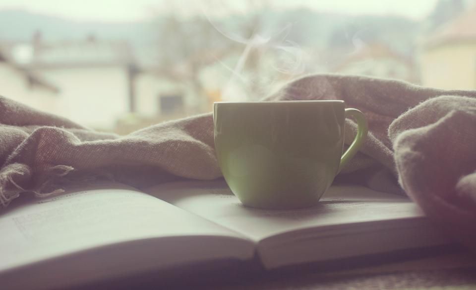 Steaming cup of tea next to an open book and blanket, a restful moment