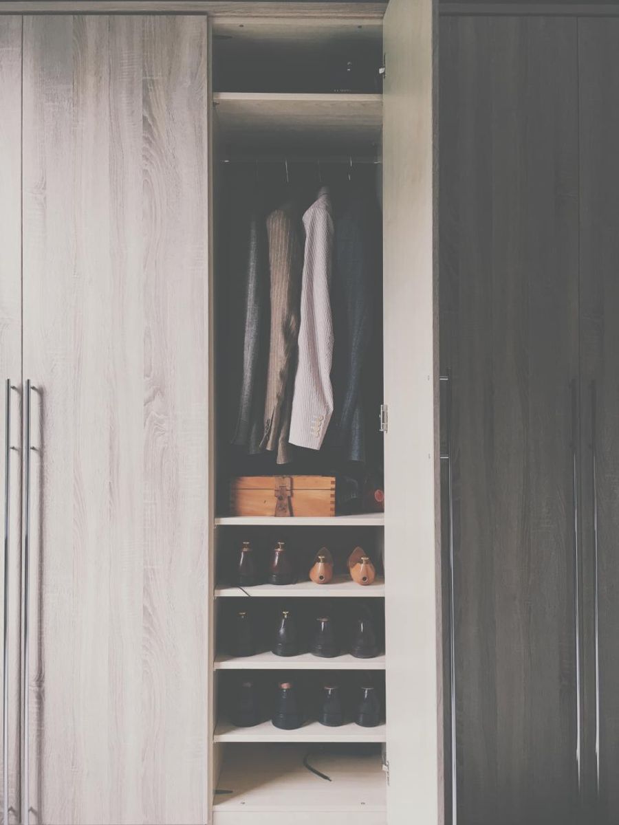 Tidy wardrobe closet with hanging clothes and shoes on shelves