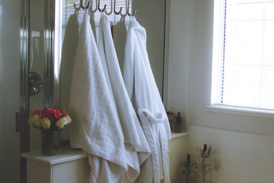 White bathrobes hanging on hooks by a bright window, a calm spa-style bathroom