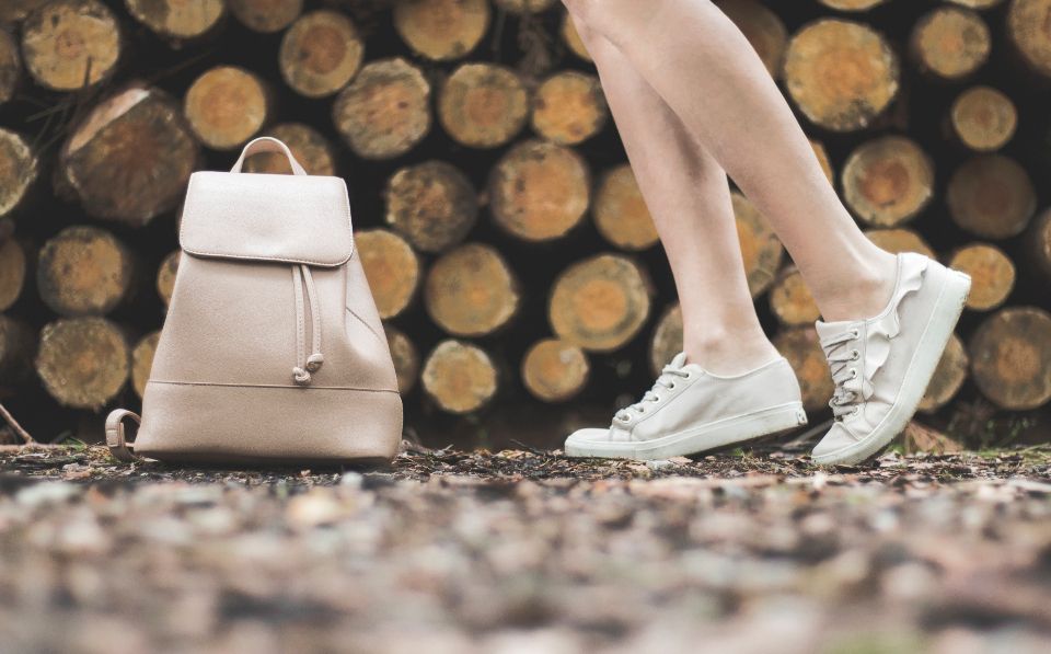White sneakers and a small white backpack against a stack of logs
