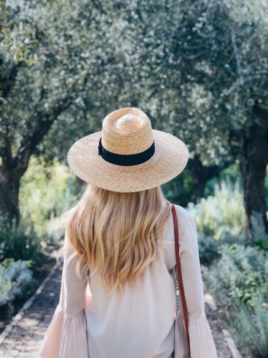 Woman with long hair seen from behind wearing a straw hat in a green garden