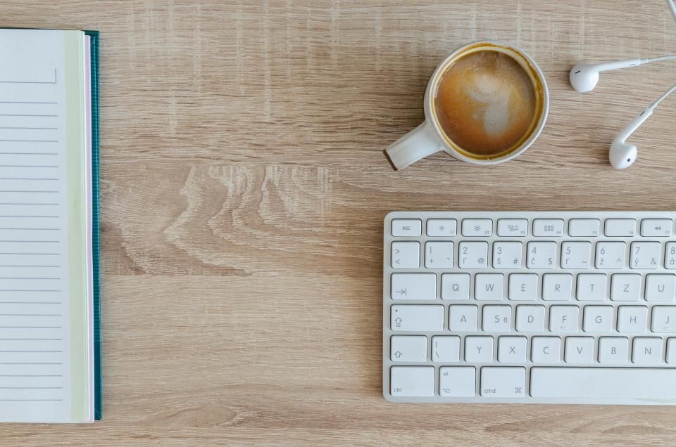 Wooden desk with notebook, coffee cup, earphones and keyboard, items for a work bag
